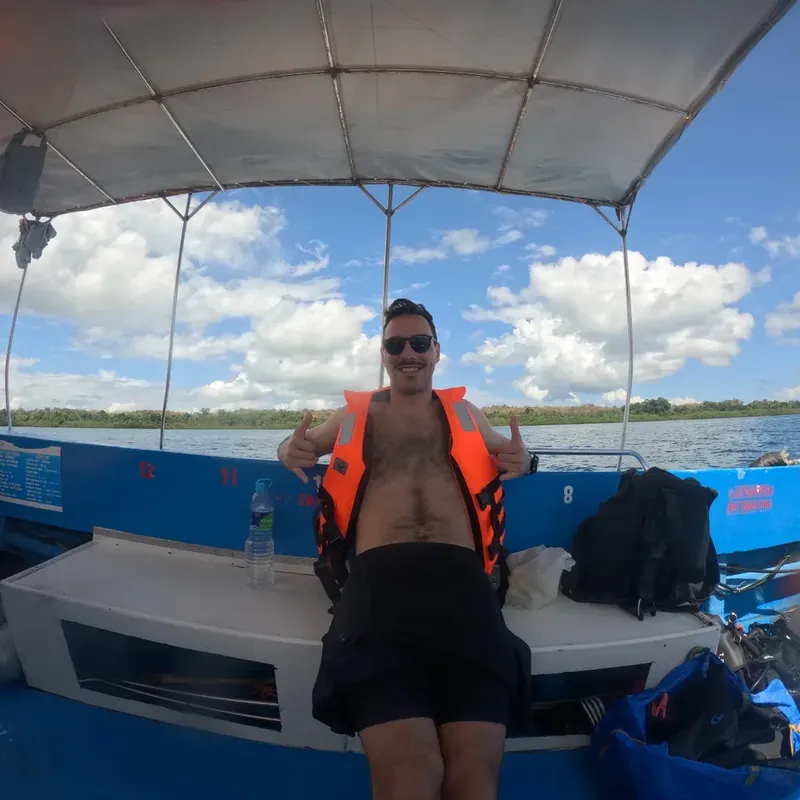 Un homme souriant fait un signe de pouce sur un bateau