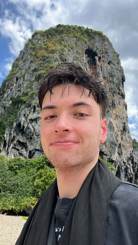 Portrait d'un homme souriant devant une falaise rocheuse tropicale
