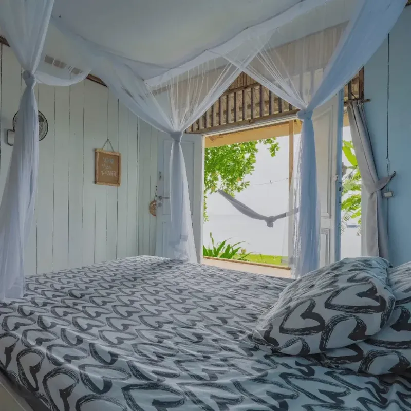 Chambre avec lit recouvert de motifs, moustiquaire et vue sur végétation