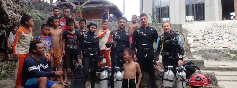 Groupe de plongeurs et enfants souriants devant un bâtiment et du matériel