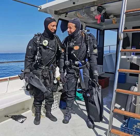 Deux plongeurs en combinaison complète sourient sur un bateau en mer
