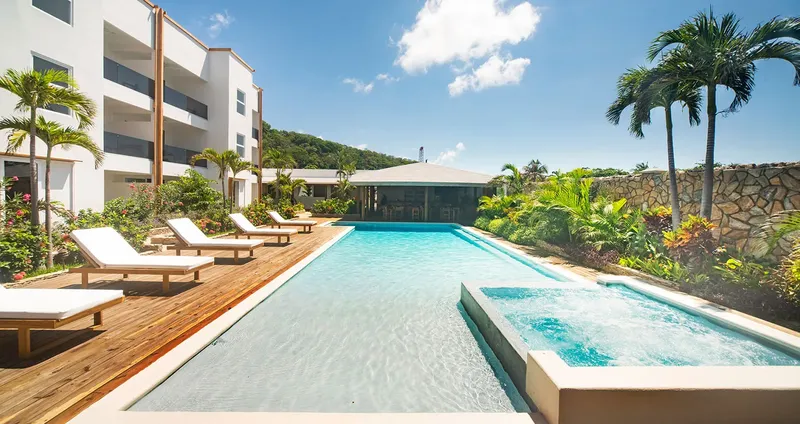 Piscine et bâtiments blancs entourés de végétation tropicale ensoleillée