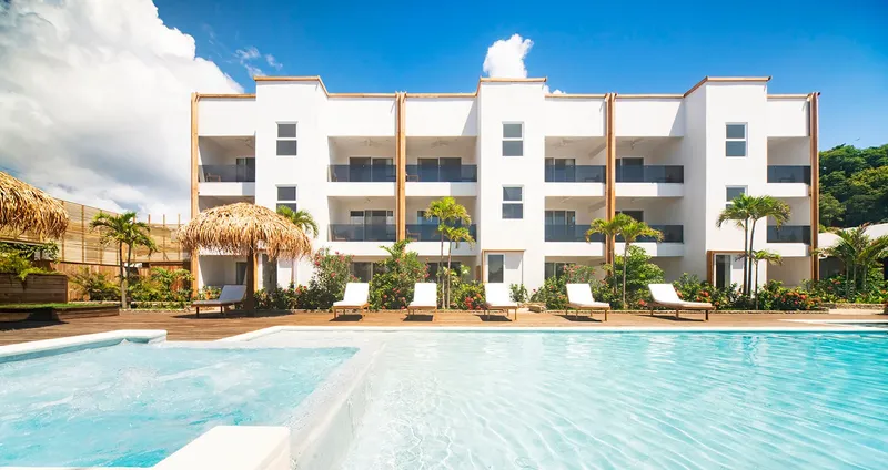 Bâtiment blanc avec piscine, transats et végétation tropicale ensoleillée