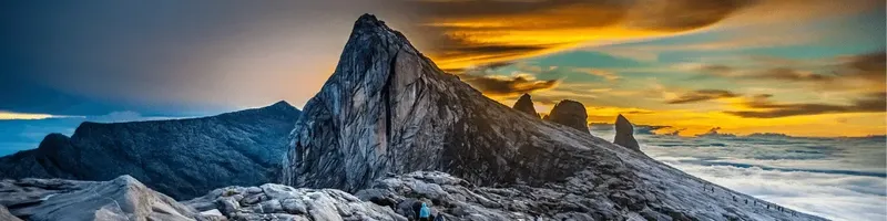 Sommet rocheux escarpé avec une personne au loin, ciel coloré