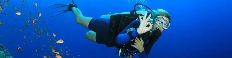 Plongeuse en combinaison regarde vers la caméra dans l'eau bleue