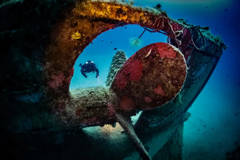 Plongeur explorant l'épave d'un navire, lumière filtrant à travers l'ouverture