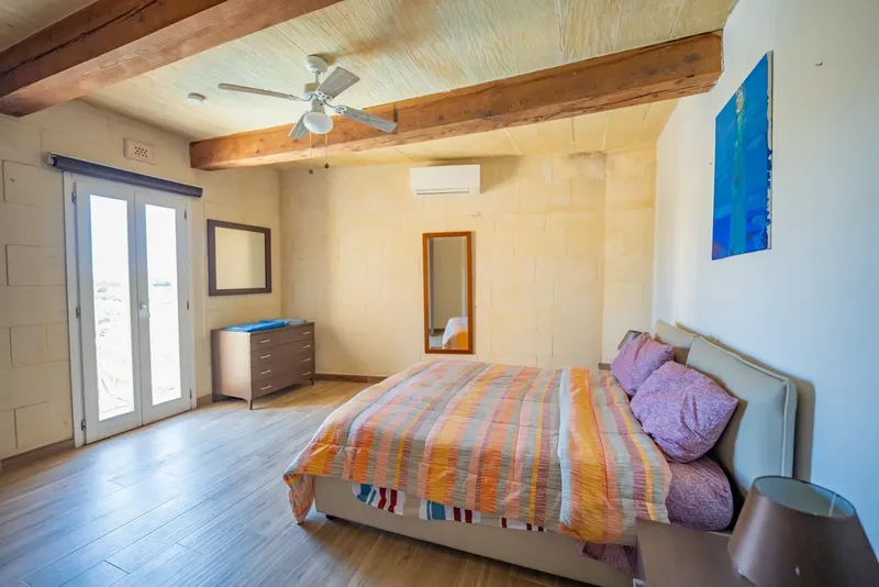 Chambre lumineuse avec lit fait, commode et poutres apparentes