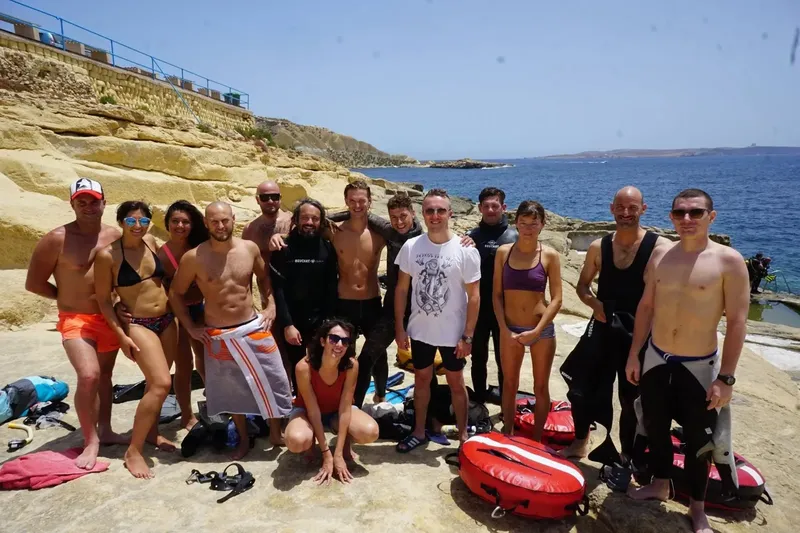 Groupe de plongeurs souriants posant sur des rochers au bord de la mer