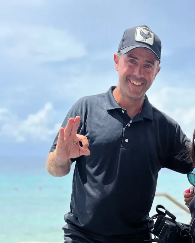 Homme souriant avec un signe OK devant une mer turquoise