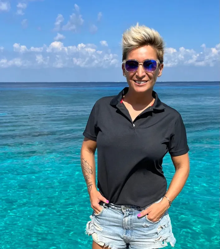 Femme souriante en short et polo devant une mer turquoise