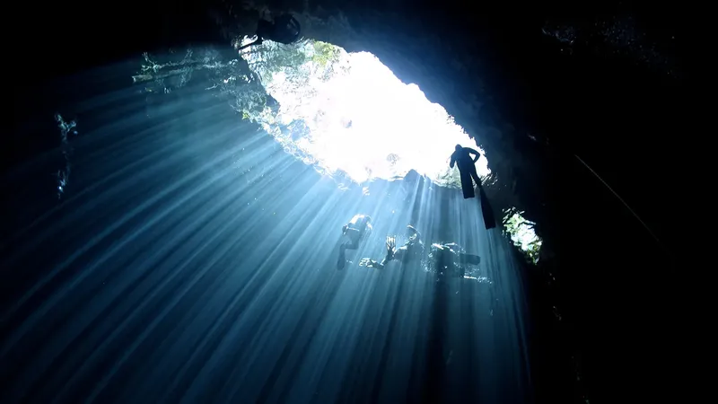 Plongeurs explorant une grotte sous-marine éclairée par un rayon de soleil