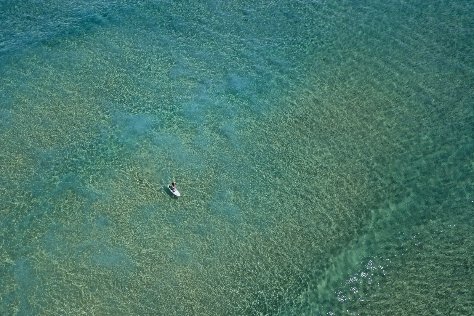 Plongeur seul, vue aérienne, eau turquoise et sable clair.
