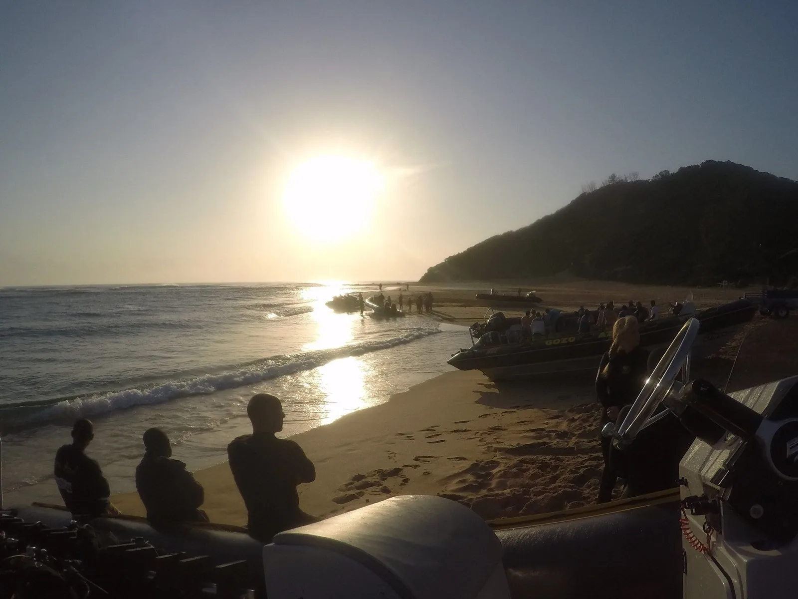 Plage, bateaux de plongée, personnes, soleil couchant, ambiance détendue.