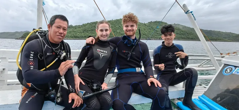 Quatre plongeurs souriants posent sur un bateau avant une immersion