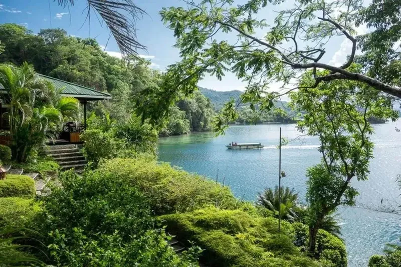 Bateau sur une baie turquoise, végétation luxuriante et bâtiments côtiers