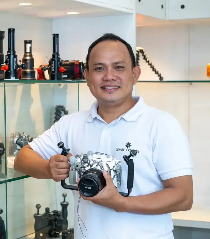 Un homme souriant tient un appareil photo sous-marin devant des lampes