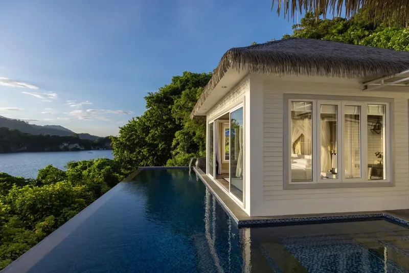 Vue d'une piscine à débordement avec une maison blanche et la mer