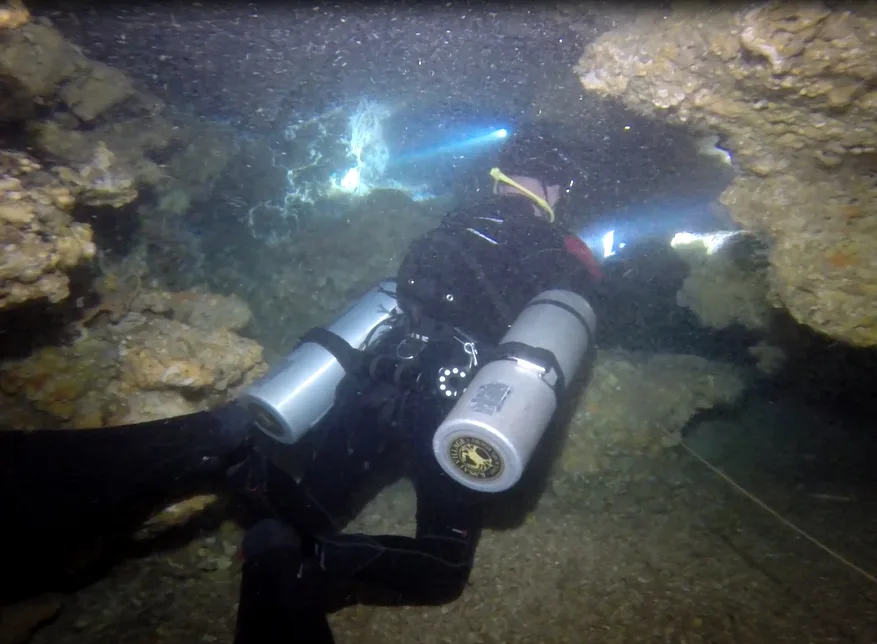 Plongeur explore une grotte sous-marine avec deux bouteilles et lampe