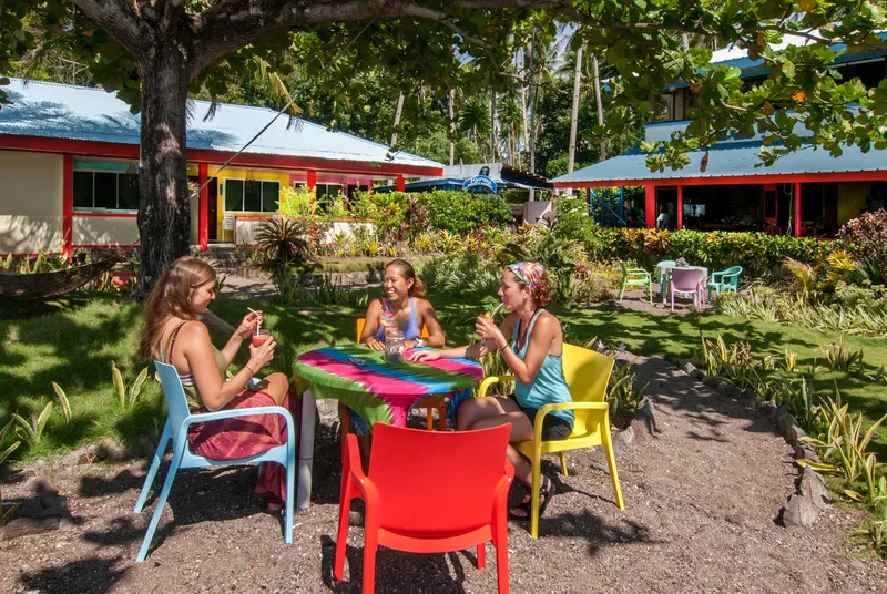 Trois personnes assises autour d'une table colorée dans un jardin tropical