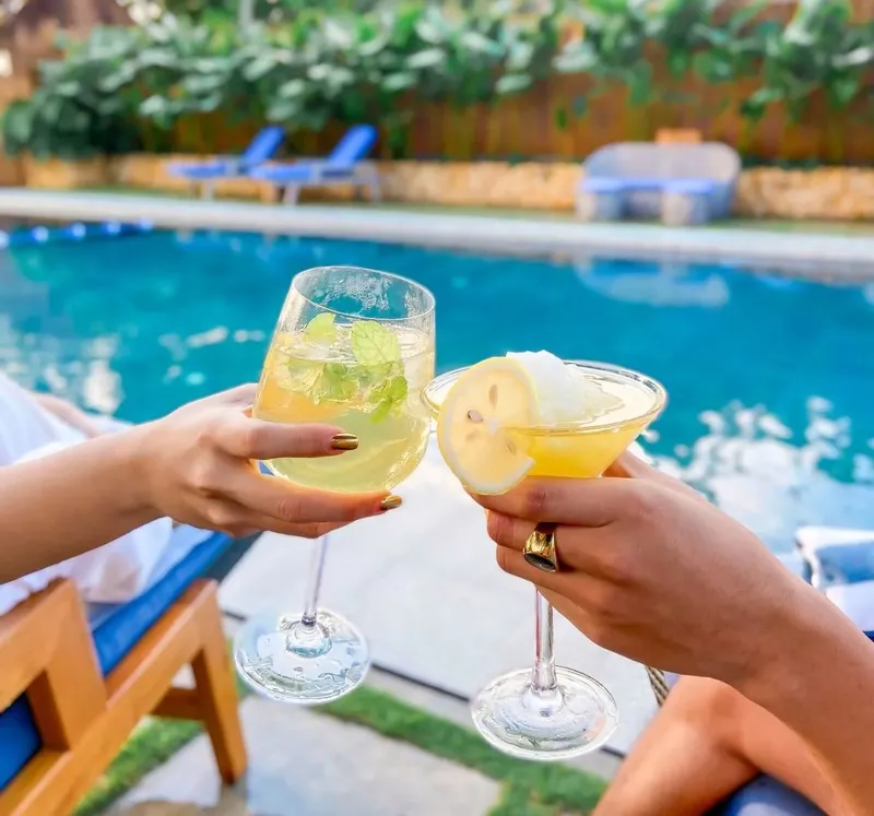 Deux personnes trinquent avec des verres colorés au bord d'une piscine
