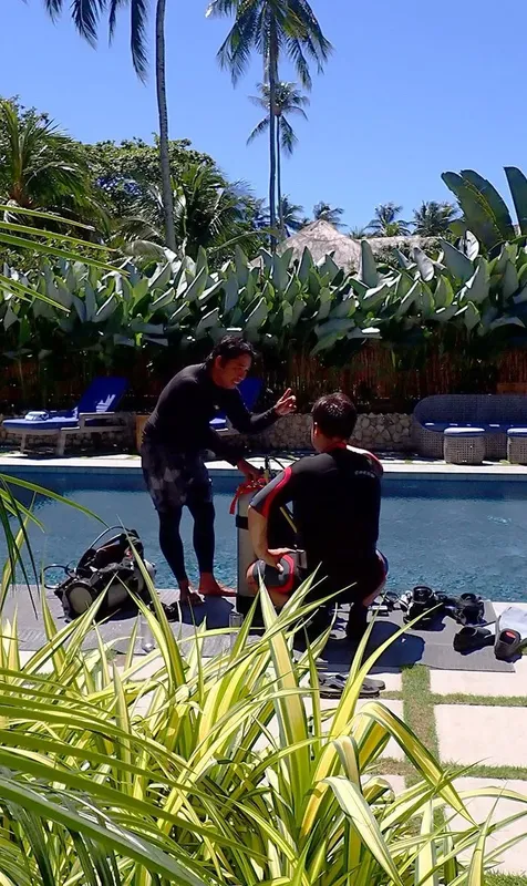 Deux plongeurs équipés discutent près du matériel au bord d'une piscine
