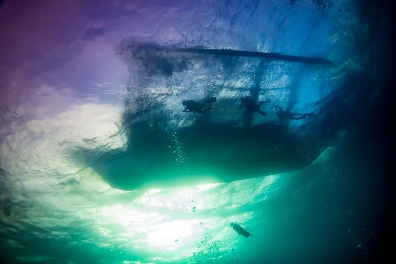 Plongeurs sous un bateau, lumière filtrée, vue d'en bas, exploration marine