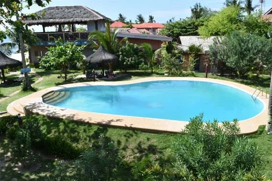 Piscine extérieure entourée de végétation luxuriante et bâtiments tropicaux