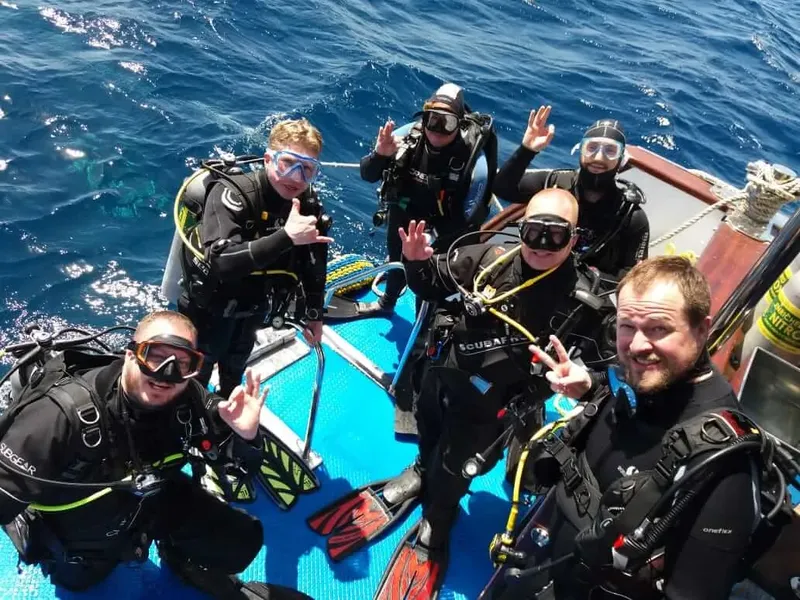 Plongeurs souriants sur un bateau bleu, équipés et prêts à plonger