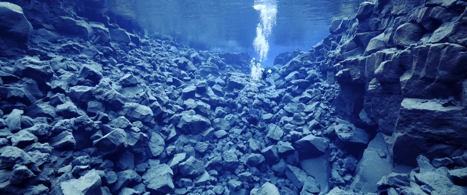 Plongeur explorant un paysage rocheux sous-marin avec une lumière descendante