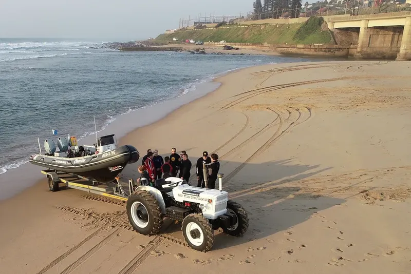 Groupe de plongeurs sur une plage avec un bateau et un tracteur