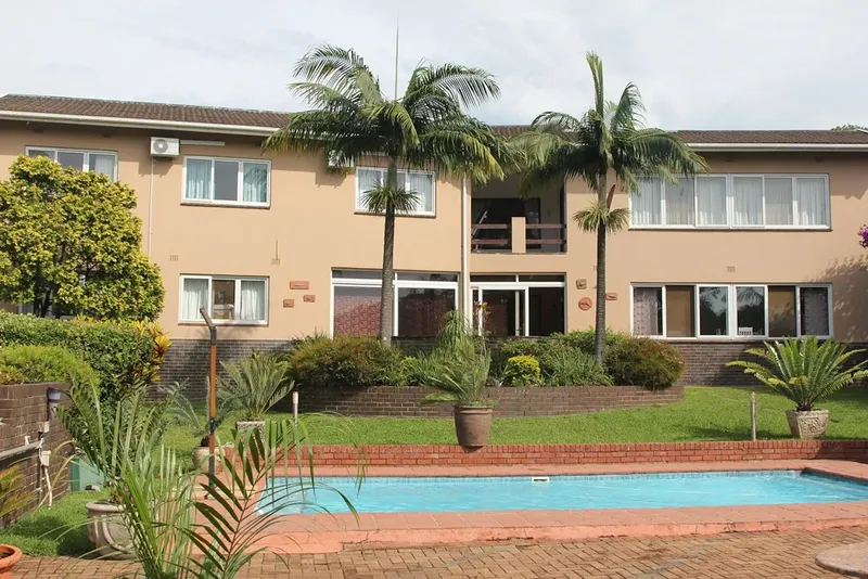Bâtiment beige à deux étages avec piscine et végétation tropicale