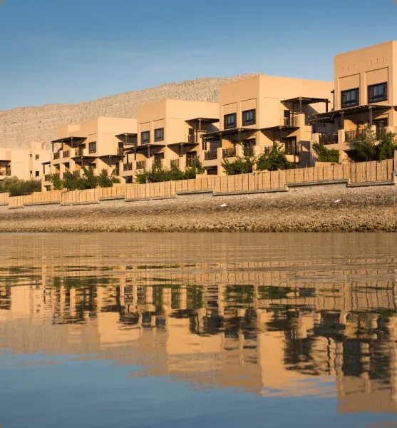 Batiments beiges avec balcons, reflet dans l'eau calme et montagne