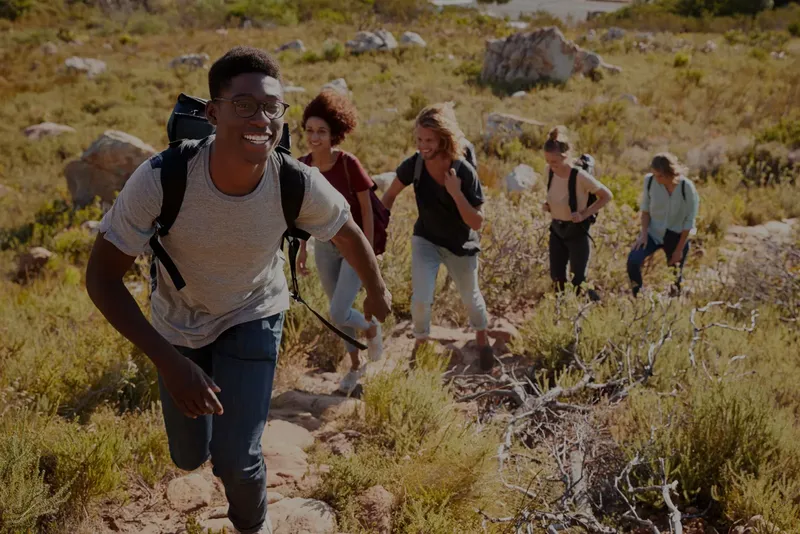 Groupe de jeunes adultes souriants marchant sur un sentier rocheux
