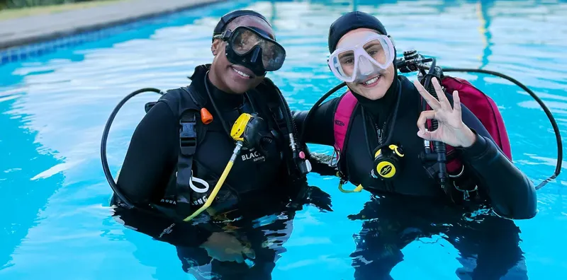 Deux plongeurs souriants en équipement complet près d'une piscine