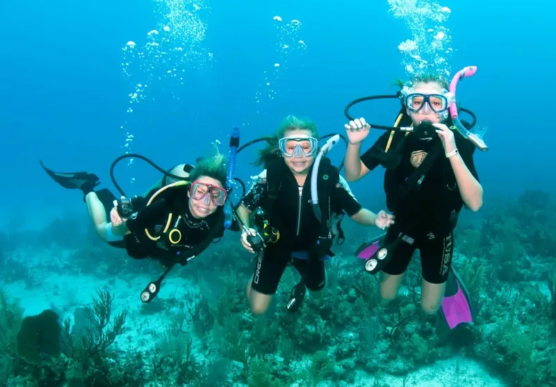 Trois plongeuses souriantes en combinaison, palmes et masques sous l'eau
