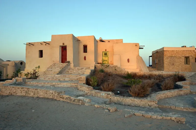 Bâtiment blanc et beige avec des ouvertures colorées et végétation sèche