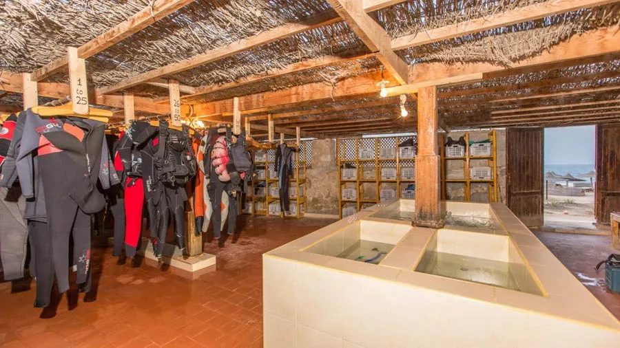 Combinaisons de plongée et matériel rangés dans un local ombragé ouvert sur la mer