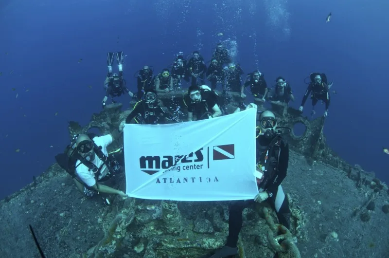 Groupe de plongeurs souriants tenant un drapeau avec un logo