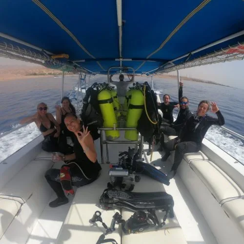 Groupe de plongeurs souriants sur un bateau en mer, équipement visible