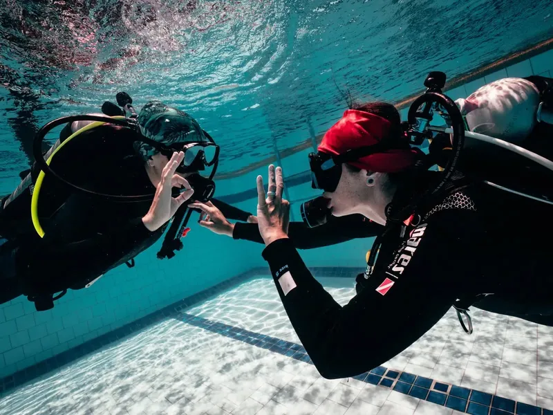 Deux plongeurs communiquent sous l'eau dans une piscine carrelée