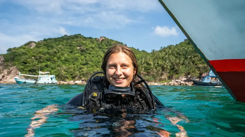 Plongeuse souriante avec son équipement, en mer devant une île