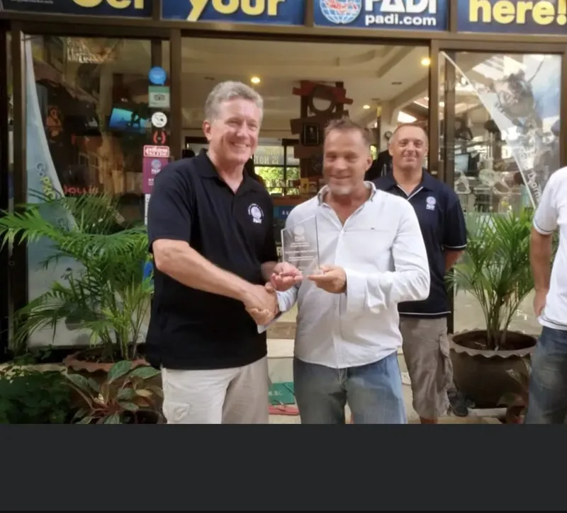 Trois hommes souriants présentent un trophée devant une vitrine