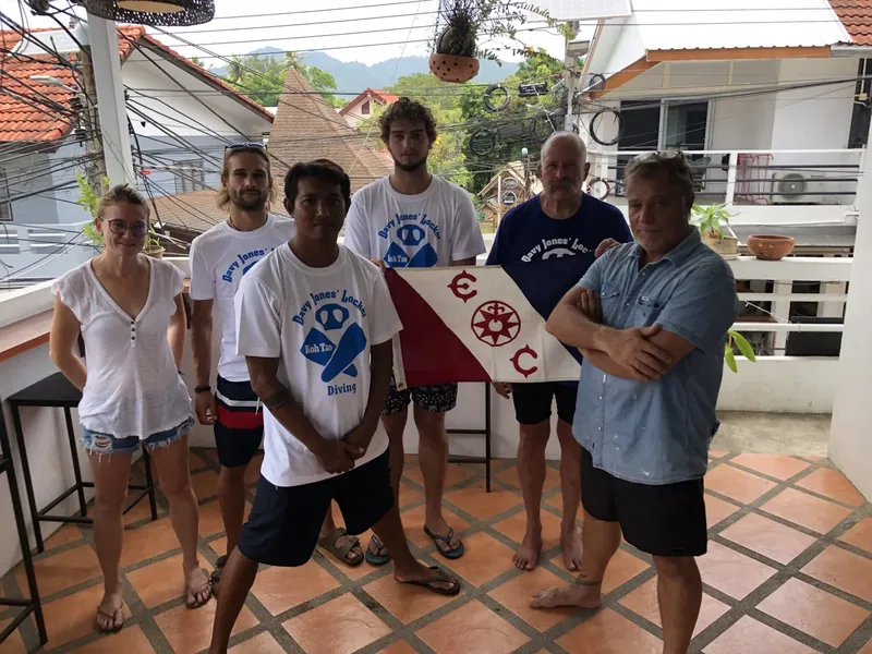 Groupe de personnes souriantes posant devant une rambarde et des drapeaux