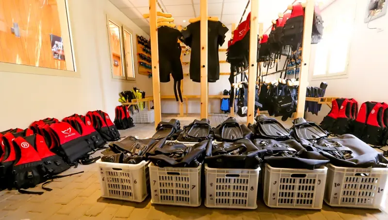 Rangées de gilets de sauvetage, combinaisons et palmes dans un local de plongée