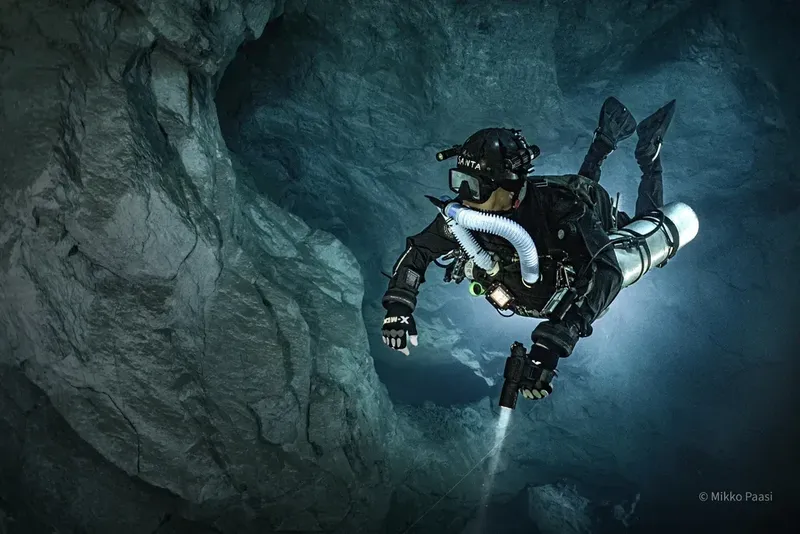 Plongeur explore une grotte sous-marine sombre et rocheuse avec équipement