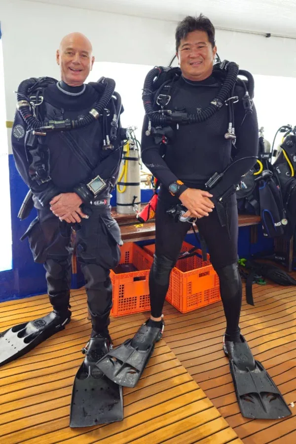 Deux plongeurs équipés sourient, debout sur une plateforme en bois