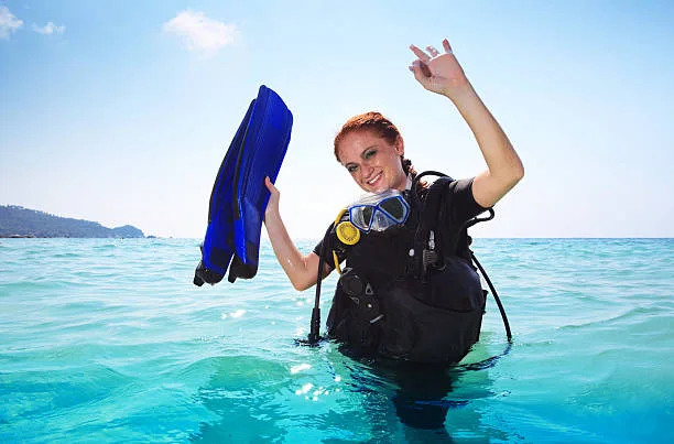 Plongeuse souriante en combinaison, tenant ses palmes dans l'eau