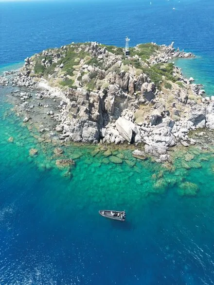 Île rocheuse avec un phare et un petit bateau en mer