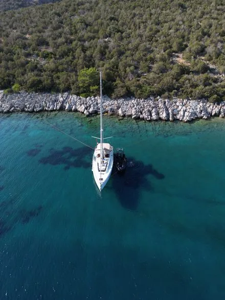Voilier blanc naviguant dans une eau turquoise près d'une côte rocheuse