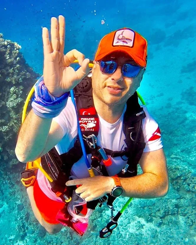 Plongeur souriant avec signe OK, lunettes de soleil et casquette rouge